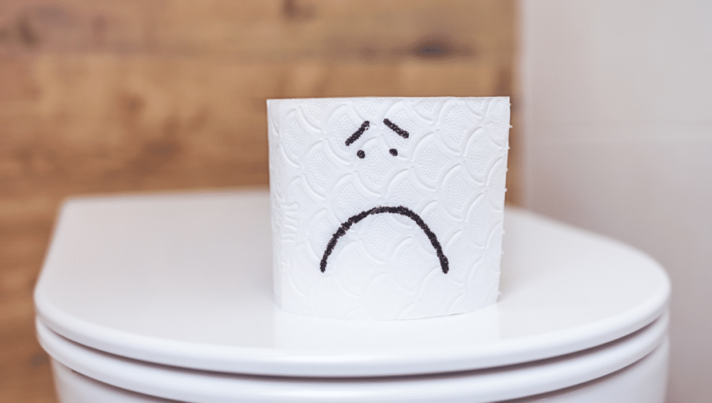 Beitragsbild zum Thema Verstopfung: Eine Klorolle mit einem traurigen Gesicht auf einem geschlossenen Toilettendeckel.