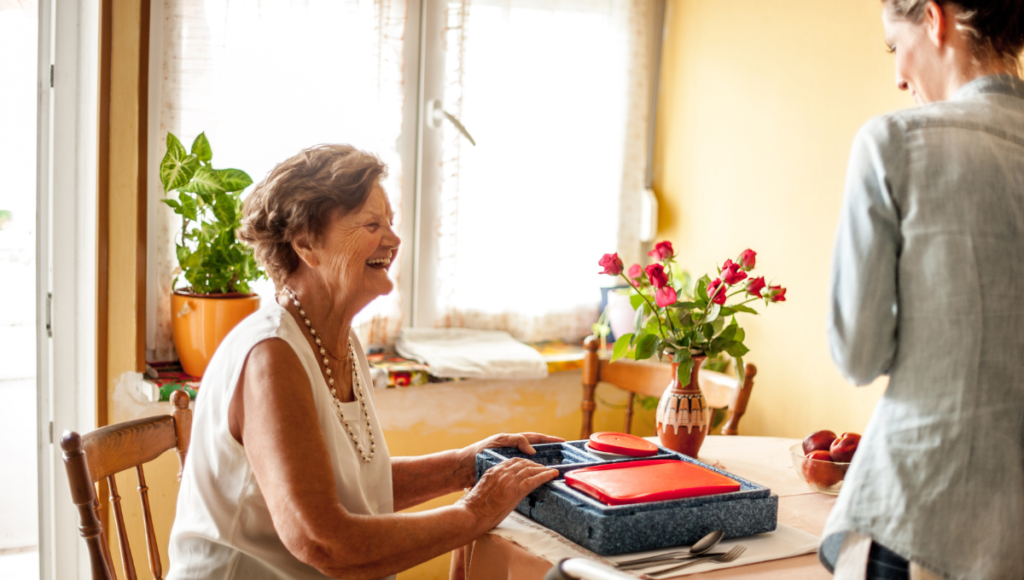 Eine Seniorin erhält von einem Menüservice Essen auf Rädern.