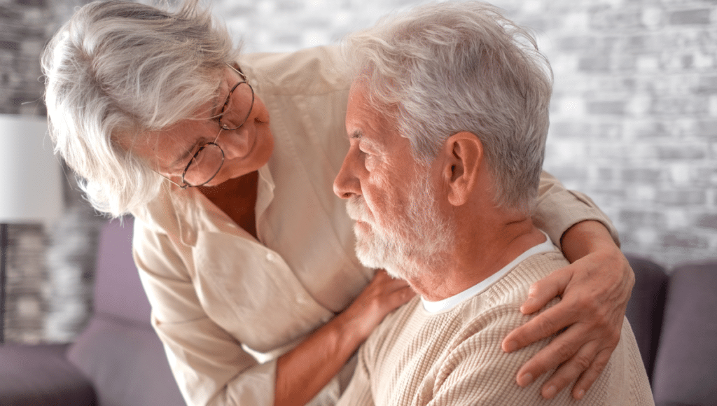 Parkinson-Demenz: Eine ältere Frau legt einem ins Leere schauenden älteren Mann tröstend die Hände auf die Schultern.