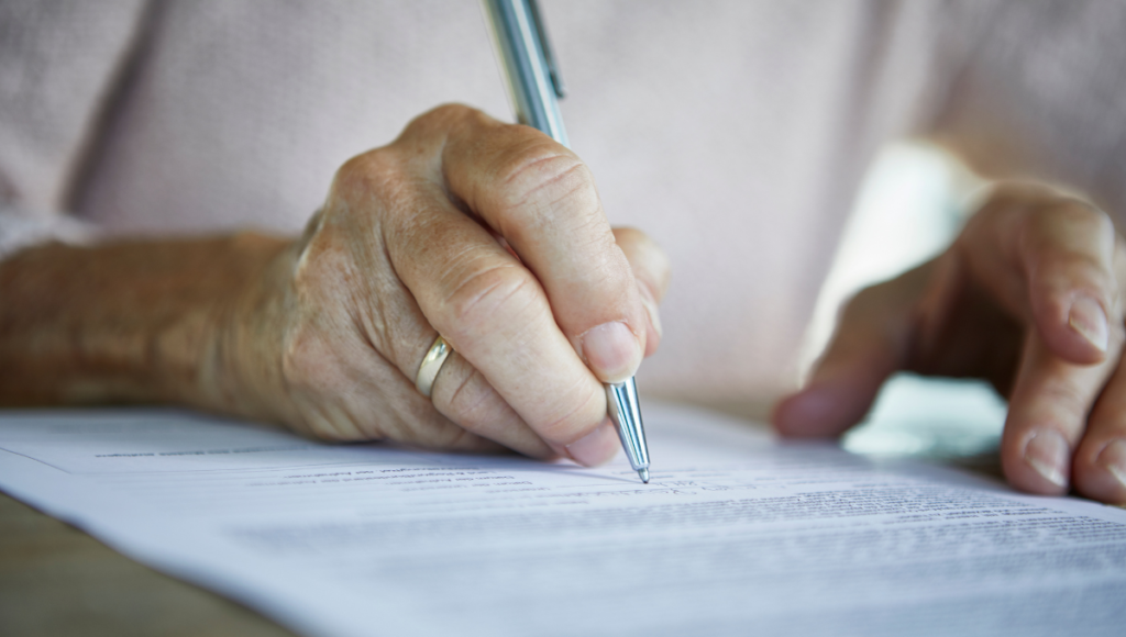 Eine Seniorin unterschreibt mit einem Kugelschreiber ihre Patientenverfügung.