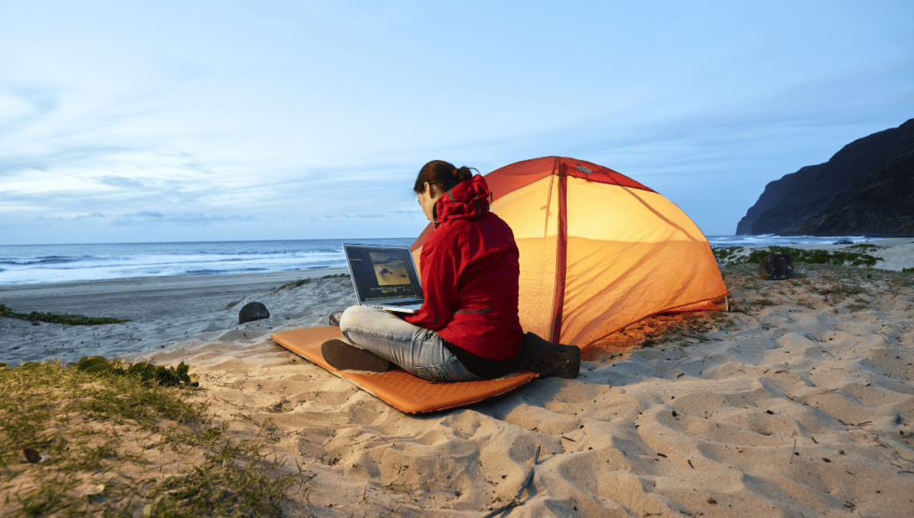 Eine Frau sitzt mit Laptop am Strand. Sie reist trotz Multipler Sklerose.