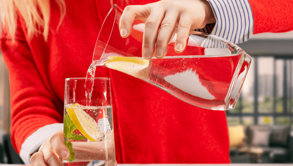 Eine Frau schenkt ein Glas Wasser ein, denn Trinken bei Hitze ist wichtig.