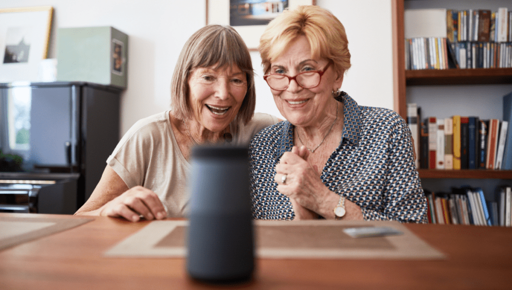 Zwei ältere Damen sitzen an einem Tisch und probieren ein Smart Home System aus.