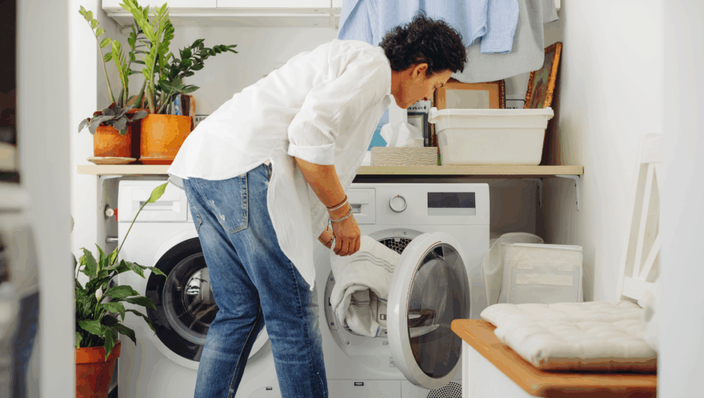 Eine Frau befüllt die Waschmaschine mit Wäsche. Das steht für Hygiene im Haushalt.